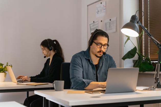 İki müşteri hizmetleri temsilcisi kulaklıkla laptoplarda çalışırken